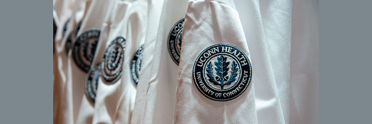 rack of white coats with UConn Health shoulder patch